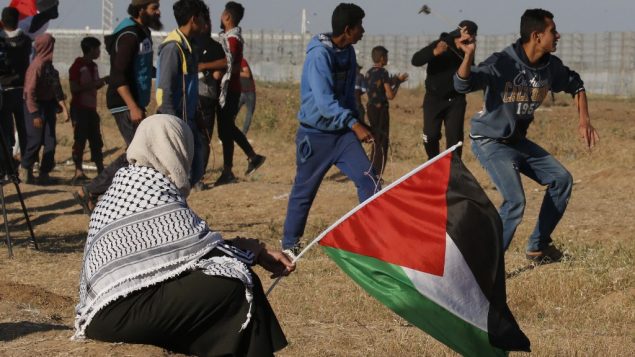متظاهر يرشق حجارة باتجاه جنود اسرائيليين بينما تحمل امرأة علم فلسطين، خلال مظاهرة بالقرب من الحدود مع اسرائيل، شرقي مدينة غزة، 10 مايو 2019 (Said KHATIB / AFP)