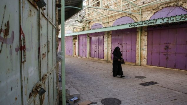 سيدة فلسطينية تمشي بين متاجر مغلقة خلال اضراب احتجاجا على قانون الضمان الاجتماعي الذي اقترحته السلطة الفلسطينية، في مدينة الخليل في الضفة الغربية، 15 يناير 2019 (HAZEM BADER / AFP)