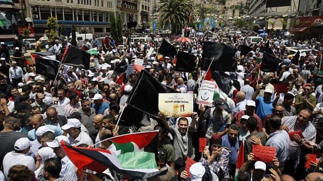 متظاهرون فلسطينيون يرفعون لافتات وأعلام فلسطين خلال تظاهرة ضد المؤتمر الاقتصادي المنعقد في البحرين برعاية أمريكية، في مدينة نابلس بالضفة الغربية، 25 يونيو، 2019.  (Jaafar Ashtiyeh/AFP)