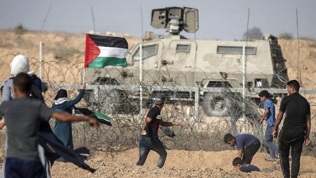 متظاهرون فلسطينيون يلقون الحجارة باتجاه القوات الإسرائيلية خلال مظاهرات عند الحدود مع اسرائيل، شرقي خان يونس، جنوب قطاع غزة، 12 يوليو 2019 (Mahmud Hams/AFP)