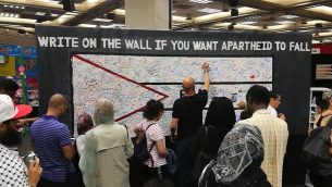 الحضور في ’معرض فلسطين 2017’ في لندن يكتبون على جدار للاحتجاج على ’الأبرتهايد’ الإسرائيلي.  (Screenshot YouTube)