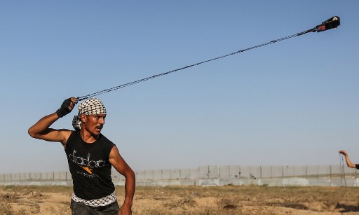 متظاهر فلسطيني يستخدم مقلاعا لرشق الحجارة باتجاه القوات الإسرائيلية بالقرب من السياج الحدودي بين اسرائيل وقطاع غزة، 16 اغسطس 2019 (MAHMUD HAMS / AFP) متظاهر فلسطيني يستخدم مقلاعا لرشق الحجارة باتجاه القوات الإسرائيلية بالقرب من السياج الحدودي بين اسرائيل وقطاع غزة، 16 اغسطس 2019 (MAHMUD HAMS / AFP)