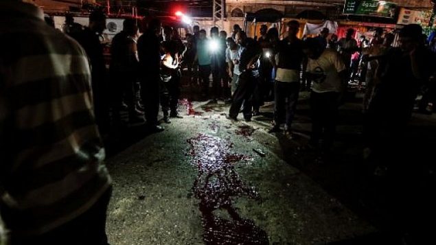فلسطينيون يتفرجون على بقع دموية على الأرض بعد هجوم بالقرب من حاجز شرطة في مدينة غزة في 27 أغسطس، 2019. ( MAHMUD HAMS / AFP)