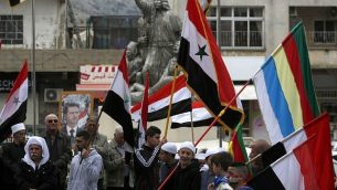 توضيحية: سكان هضبة الجولان يلوحون بالأعلام السورية ويقفون أمام صورة للرئيس السوري بشار الأسد خلال تظاهرة ضد اعتراف الرئيس الأمريكي دونالد ترامب بالسيادة الإسرائيلية على المنطقة المتنازع عليها، في بلدة مجدل شمس، 23 مارس، 2019.  (Jalaa Marey/AFP)