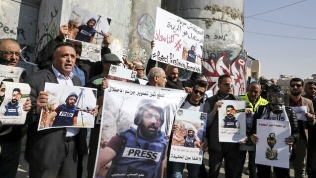 صحافيون فلسطينيون يغطون عيونهم بلاصق خلال تظاهرة أقيمت من أمام الجدار الفاصل في بيت لحم بالضفة الغربية، 17 نوفمبر، 2019، يحملون لافتاتتضامنا مع  تضمانا مع المصور الفلسطيني معاذ عمارنة، الذي أصيب قبل أيام من ذلك برصاصة مطاطية في عينه خلال تغطيته لاشتباكات بين متظاهرين فلسطينيين وقوات إسرائيلية في الضفة الغربية. (HAZEM BADER / AFP)