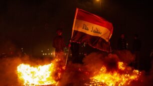 متظاهر عراقي مناهض للحكومة يحمل العلم الوطني وهو يقف بجانب النار عند حاجز مؤقت في مدينة البصرة الجنوبية، 25 ديسمبر 2019. (Hussein FALEH / AFP)