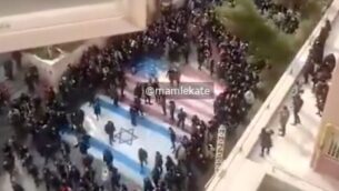 لقطة شاشة من شريط فيديو يظهر على ما يبدو متظاهرون إيرانيين مناهضين للنظام يرفضوا الدوس على أعلام الولايات المتحدة وإسرائيل في مظاهرة بجامعة في طهران، 12 يناير 2020. (Twitter)