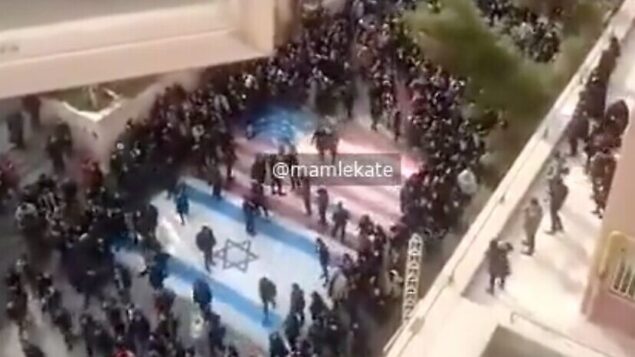 لقطة شاشة من شريط فيديو يظهر على ما يبدو متظاهرون إيرانيين مناهضين للنظام يرفضوا الدوس على أعلام الولايات المتحدة وإسرائيل في مظاهرة بجامعة في طهران، 12 يناير 2020. (Twitter)