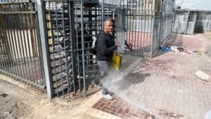 عمال صحة فلسطينيون يقومون بإجراء تعقيم لعمال فلسطينيين عائدين من إسرائيل عند حاجز في ترقوميا، ٫ 25 مارس، 2020. (Wisam Hashlamoun/Flash90)