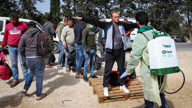 عمال صحة فلسطينيون يقومون بإجراء تعقيم للعمال الفلسطينين العائدين من إسرائيل إلى الضفة الغربية عند حاجر في ترقوميا، 27 مارس، 2020.(Wisam Hashlamoun/Flash90)