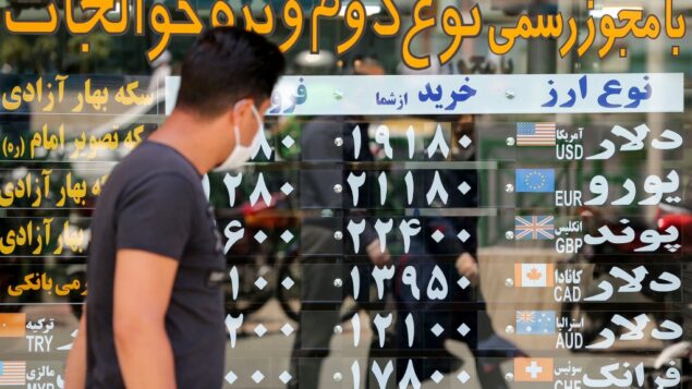 رجل يرتدي قناعًا بسبب فيروس كورونا يتحقق من أسعار صرف العملات وهو يمشي في العاصمة الإيرانية طهران، 22 يونيو 2020 (ATTA KENARE / AFP)