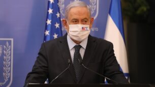 رئيس الوزراء بنيامين نتنياهو يرتدي قناع وجه ضد حماية من كوفيد-19 يحمل العلمين الأمريكي والإسرائيلي، خلال مؤتمر صحفي مع الممثل الأمريكي الخاص لإيران (لا يظهر) في مكتب رئيس الوزراء في القدس، 30 يونيو 2020. (Abir Sultan/POOL/AFP)