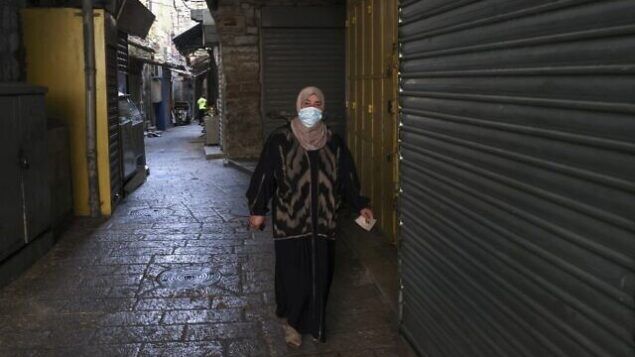 امرأة فلسطينية ترتدي قناعا واقيا تمشي في شارع فارغ تصطف على جانبيه المحلات التجارية المغلقة في البلدة القديمة بالقدس، خلال إغلاق في جميع أنحاء البلاد بسبب فيروس كورونا، 19 سبتمبر 2020 (Menahem Kahana/AFP) امرأة فلسطينية ترتدي قناعا واقيا تمشي في شارع فارغ تصطف على جانبيه المحلات التجارية المغلقة في البلدة القديمة بالقدس، خلال إغلاق في جميع أنحاء البلاد بسبب فيروس كورونا، 19 سبتمبر 2020 (Menahem Kahana/AFP)