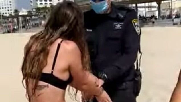 شرطي يكبل يدي شابة على أحد شواطئ تل أبيب بعد أن رفضت الكشف عن هويتها لعناصر الشرطة الذين حاولوا تغريمها بسبب عدم ارتدائها للكمامة، 9 أكتوبر ، 2020. (Screen grab)