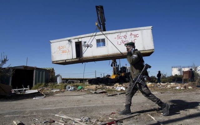 An Israeli border policeman walks near workers lifting a housing unit with a crane during the demolition of Amona on Tuesday. Photo: EPA/Abir Sultan An Israeli border policeman walks near workers lifting a housing unit with a crane during the demolition of Amona on Tuesday. Photo: EPA/Abir Sultan