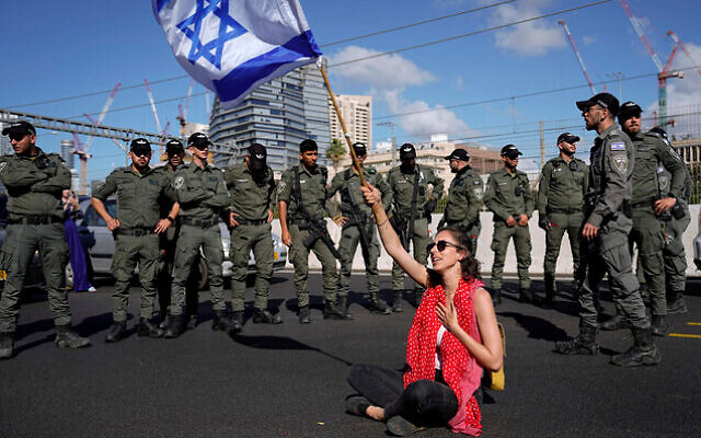 A demonstrator waves the Israeli flag seated on a highway while flanked by paramilitary border police during a protest against plans by Prime Minister Benjamin Netanyahu's government to overhaul the judicial system, in Tel Aviv, Israel, Thursday, March 9, 2023. (AP Photo/Ariel Schalit) A demonstrator waves the Israeli flag seated on a highway while flanked by paramilitary border police during a protest against plans by Prime Minister Benjamin Netanyahu's government to overhaul the judicial system, in Tel Aviv, Israel, Thursday, March 9, 2023. (AP Photo/Ariel Schalit)