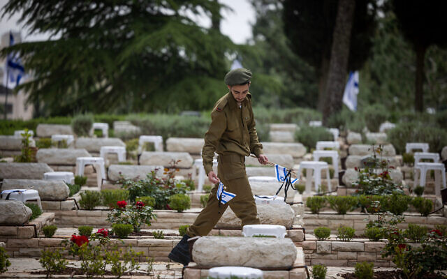 An Israeli soldier places flags, flowers and candles on graves of fallen soldiers at the Mount Herzl Military Cemetery in Jerusalem, April 23, 2023, ahead of Memorial Day. (Yonatan Sindel/Flash90) An Israeli soldier places flags, flowers and candles on graves of fallen soldiers at the Mount Herzl Military Cemetery in Jerusalem, April 23, 2023, ahead of Memorial Day. (Yonatan Sindel/Flash90)