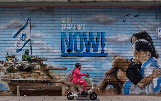 A woman rides a scooter past a graffiti calling for the return of the hostages kidnapped during the Oct. 7 Hamas cross-border attack in Israel, in Kfar Saba, Israel, Monday, Feb. 26, 2024. (The Times of Israel: AP/Ohad Zwigenberg) A woman rides a scooter past a graffiti calling for the return of the hostages kidnapped during the Oct. 7 Hamas cross-border attack in Israel, in Kfar Saba, Israel, Monday, Feb. 26, 2024. (The Times of Israel: AP/Ohad Zwigenberg)