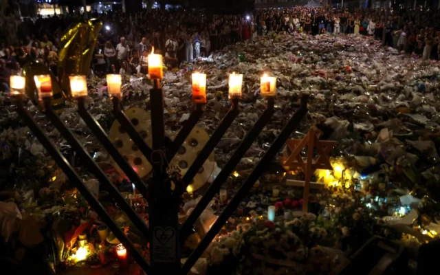 A menorah is pictured after the seventh candle is lit for the Jewish festival of Hanukkah as mourners stand next to floral tributes laid out in memory of the victims of a shooting attack at Bondi Beach, in Sydney, December 20, 2025. (David Gray / AFP) A menorah is pictured after the seventh candle is lit for the Jewish festival of Hanukkah as mourners stand next to floral tributes laid out in memory of the victims of a shooting attack at Bondi Beach, in Sydney, December 20, 2025. (David Gray / AFP)