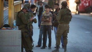 جندي إسرائيلي يتفحص هوية شاب فلسطيني عند نقطة تفتيش في بلدة الخليل بالضفة الغربية،  15 يونيو 2014، AFP PHOTO / مناحيم كاهانا