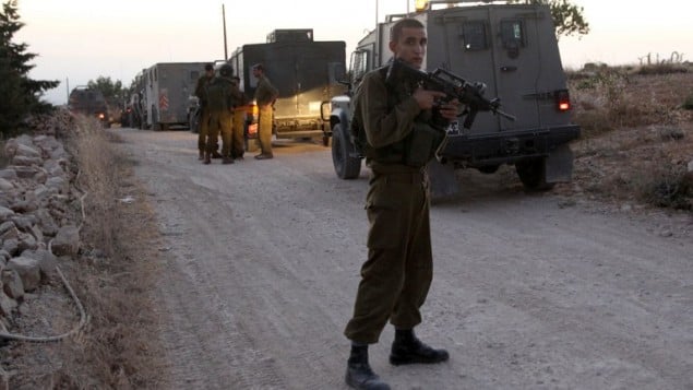 توضيحية: جندي اسرائيلي يحرس مدخل قرية حلحول بعد حظر التجول  30 يونيو 2014 (AFP PHOTO/ HAZEM BADER)