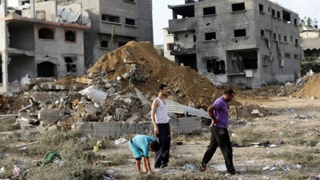 رجال فلسطينيون يقفون وسط أنقاض المباني في اعقاب غارة جوية إسرائيلية، أسفرت عن مقتل 18 شخصا من عائلة واحدة في مدينة غزة،  13 يوليو 2014،  AFP PHOTO