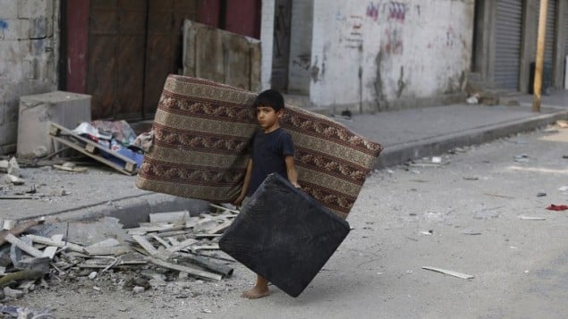 صبي فلسطيني يمشي وسط الحطام في شارع مهجور في وسط مدينة غزة، ويحمل فراش  في محاولة لانقاذ ما تبقى من الشقة المهدومة عائلته22 يوليو 2014.  AFP PHOTO / MOHAMMED ABED