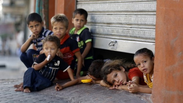 الأطفال الفلسطينيون المنزاحون يطلون من تحت باب مكان تحتمي به أسرهم في مدينة غزة 26 يوليو 2014.  AFP PHOTO / MOHAMMED ABED