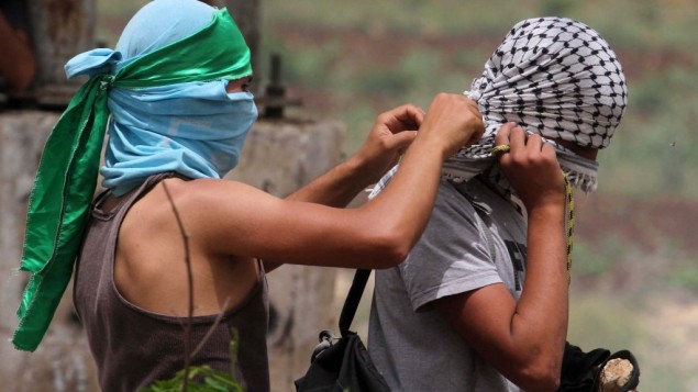 فلسطيني يلبس عقال اخضر  بصفته مؤيدا لحماس، ويساعد زميل متظاهر تغطية وجهه بحطة سوداء وبيضاء والتي أصبحت رمزا لحركة فتح . خارج سجن عوفر، العسكري الاسرائيلي بالقرب من مدينة الضفة الغربية رام الله، الأربعاء، 4 يونيو، 2014 (صعام ريماوي/ فلاش 90 )