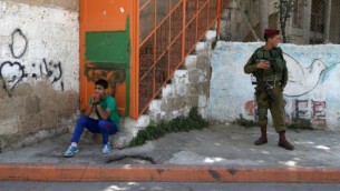 صبي فلسطيني يجلس بالقرب من الجنود الاسرائيليين المنتشرين في مدينة الخليل بالضفة الغربية، في أول جمعة من شهر رمضان  Nati Shohat/FLASH90