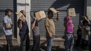 رجال فلسطينيون يحملون قطعة من الورق المقوى لحماية أنفسهم من الشمس عند وقوفهم في صف للحصول على الخبز في شارع بوسط مدينة غزة  30 يوليو 2014. AFP PHOTO / MARCO LONGARI