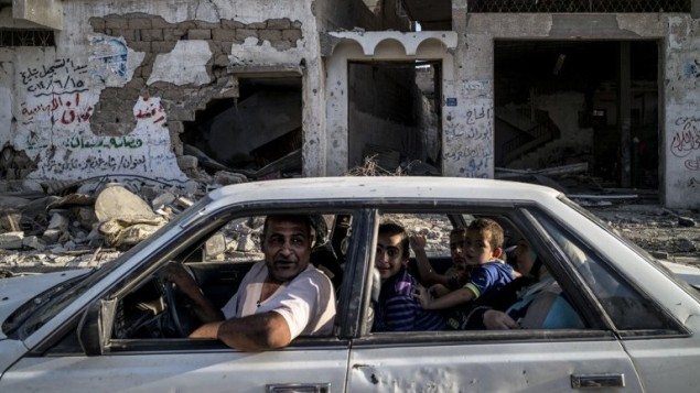 أسرة فلسطينية تسوق عبر حارة مهدمة امام مبنى مدمر في حي الشجاعية  مدينة غزة 6 أغسطس 2014.  AFP PHOTO / MARCO LONGARI