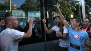 مراهقون يهود من اليمين المتطرف مع لاصقات "كهانا كان على حق" ولاصقات "انتقام" يشيرون باصابعهم الوسطى الى إمرأة مسلمة محجبة جالسة داخل القطار الخفيف في القدس. 1 يوليو 2014 (ناتي شوحاط/ فلاش 90)