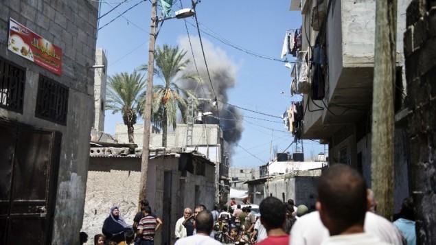 فلسطينيون يراقبون سحابة الدخان المتصاعد فوق المنازل بعد لحظات من سقوط صاروخ إسرائيلي في أرض مفتوحة بالقرب من مدينة غزة في 21 أغسطس، 2014. ( AFP/ ROBERTO SCHMIDT)