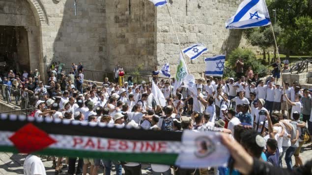 امرأة فلسطينية ترفع علم فلسطين مقابل شباب يهود يرفعون اعلام اسرائيل خلال مسيرة العلم في البلدة القديمة في القدس، 17 مايو 2015 (AFP Photo/Jack Guez)