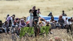 صورة مأخوذة من الجانب التركي للحدود في سوروك، محافظة سانليورفا، تظهر الجنود الأتراك وهم يحرسون الحدود في الوقت الذي ينتظر فيه أكراد سوريون وراء  السياج الشائك على الجانب السوري من الحدود بعد فرارهم من مدينة كوباني السورية، المعروفة أيضا بعين العرب، 26 يونيو، 2015.  (AFP PHOTO/BULENT KILIC)