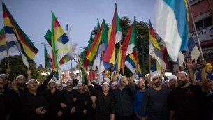 دروز إسرائيليون يلوحون بالأعلام خلال تظاهرة شارك فيها حوالي 2000 شخص في بلدة دالية الكرمل، دعوا فيها الحكومة الإسرائيلية إلى دعم ومساعدة أقربائهم في سوريا، 14 يونيو، 2015. (AFP/MENAHEM KAHANA)