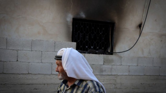 رجل فلسطيني يمر امام منزل عائلة دوابشة في بلدة دوما في الضفة الغربية، حيث أدى هجوم حريق من قبل إرهابيين يهود الى مقتل رضيع فلسطيني عمره 18 شهرا، 31 يوليو 2015 (FLASH90)