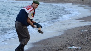 شرطي تركي يحمل جثة طفل سوري في شاطئ بدرم، جنوب تركيا، 2 سبتمبر 2015 (AFP/DOGAN NEWS AGENCY)