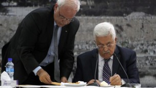 رئيس السلطة الفلسطينية محمود عباس، من اليمين، يوقع على طلب الإنضمام إلى 15 هيئة مرتبطة بالأمم المتحدة ومعاهدات دولية أخرى في المقاطعة في رام الله بالضفة الغربية يوم الثلاثاء، 1 أبريل، 2014. إلى جانبه يقف صائب عريقات. (Issam Rimawi/Flash90)