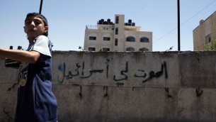 طفل فلسطيني يمر امام جدار عليه الشعار ’الموت لإسرائيل’ في حي بيت حنينا في القدس الشرقية، يوليو 2008 (Michal Fattal/Flash90)
