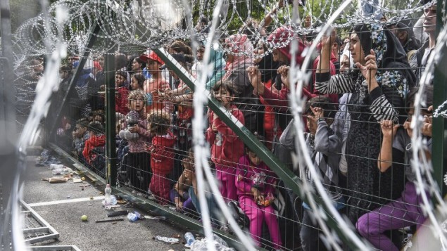 لاجئون يقفون خلف سياج على الحدود بين المجر وصربيا، 16 سبتمبر 2015 (ARMEND NIMANI / AFP)