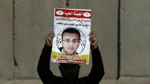 صورة تم إلتقاطها في 22 يناير، 2016، تظهر رجلا فلسطينيا يحمل لافتة تحمل صورة الصحافي الفلسطيني محمد القيق خلال تظاهرة بالقرب من رام الله للمطالبة بإطلاق سراحه من السجن الإسرائيلي. (Abbas Momani/AFP, File)