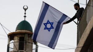 يهودي إسرائيلي يرفع العلم الإسرائيلي بالقرب من المدينة القديمة في القدس، التي شهدت تدفق سكان يهود على مناطق تسكنها أغلبية عربية. (Abir Sultan/Flash 90)