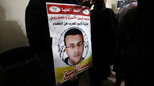 متظاهر يرفع ملصق يظهر صورة الاسير الفلسطيني المضرب عن الطعام محمد القيق خلال مظاهرة دعما له امام مكاتب اللجنة الدولية للصليب الاحمر في مدينة رام الله في الضفة الغربية، 7 فبراير 2016 (AFP / ABBAS MOMANI)