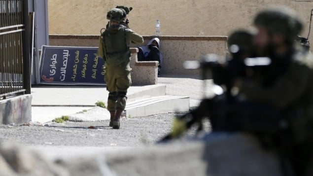 جندي اسرائيلي يوجه سلاحه نحو متظاهر فلسطيني قبل اعتقاله في مخيم الامعري بالقرب من رام الله في الضفة الغربية، 15 فبراير 2016 (ABBAS MOMANI / AFP)