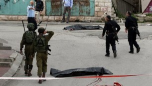 جنود إسرائيليون والشرطة يحيطون بجثتي منفذي هجوم فلسطينيين قُتلا بعد أن هاجما جندي إسرائيلي بسكين مما أدى إلى إصابته قبل أن يُقتلا بنيران الوقوات الإسرائيلية، بحسب متحدث بإسم الجيش، عند مدخل حي تل الرميدة في مدينة الخليل بالضفة الغربية، 24 مارس، 2016. (AFP / HAZEM BADER)