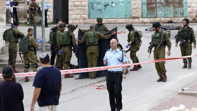 جنود اسرائيليون يغطون جثمان المعتدي الفلسطيني الذي قُتل برصاص جندي اطلق النار على رأسه بينما كان ملقى مصاب على الارض بعد طعنه جندي في الخليل، 24 مارس 2016 (AFP / HAZEM BADER)