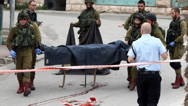 جنود إسرائيليون يحملون جثة أحد الفلسطينيين اللذين قُتلا بعد مهاجمتهما لجندي إسرائيلي في هجوم طعن قبل أن يُقتلا بنيران القوات الإسرائيلية عند مدخل حي تل الرميدة اليهودي وسط مدينة الخليل ف الضفة الغربية، 24 مارس، 2016. (AFP/Hazem Bader)