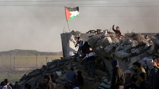 من الأرشيف: متظاهر فلسطيني يرفع العلم الفلسطيني خلال مواجهات مع القوات الإسرائيلية على الحدود مع إسرائيل في الضواحي الجنوبية لمدينة غزة في 4 ديسمبر، 2015. (AFP PHOTO/MAHMUD HAMS) من الأرشيف: متظاهر فلسطيني يرفع العلم الفلسطيني خلال مواجهات مع القوات الإسرائيلية على الحدود مع إسرائيل في الضواحي الجنوبية لمدينة غزة في 4 ديسمبر، 2015. (AFP PHOTO/MAHMUD HAMS)
